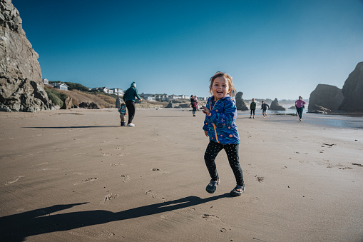 An adorable Eurasian three year old girl of Hawaiian and Chinese descent laughs and looks directly at the camera while running along a beach in Bandon, Oregon on a sunny, winter day while on vacation with her family.