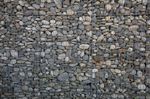 Gabion grated stone wall by pebbles in iron cage of rock horizontal stones box filled with rocks background