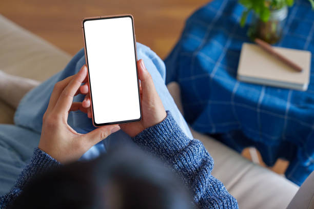 In the cropped image, an Asian woman is sitting relaxed on the sofa, using a blank screen smartphone.