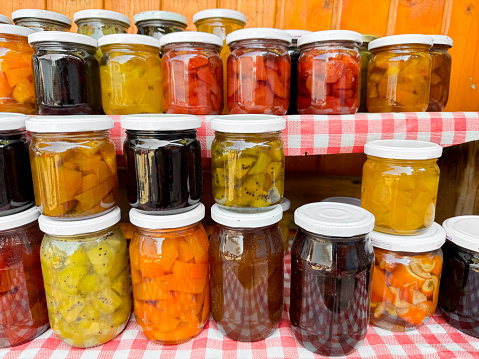 Assortment of homemade preserves in glass jars with checkered cloth, various pickled fruits and vegetables, colorful display, canned goods collection, close up with selective focus. High quality photo
