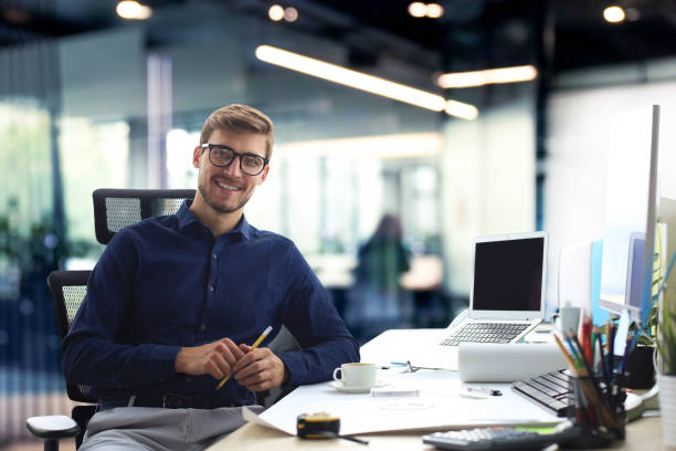 istock Handsome male architect looking at camera and smiling while sitting in the office. 2149207833