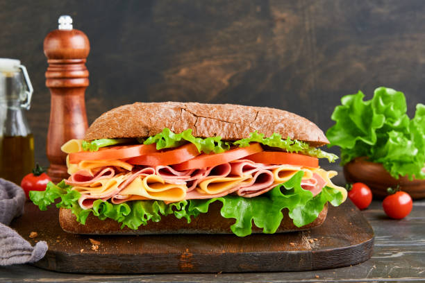 istock Sandwich. One fresh big submarine sandwich with ham, cheese, lettuce, tomatoes and microgreens on old wooden dark background. Healthy breakfast theme concept, school lunch, breakfast or snack. 2149208435