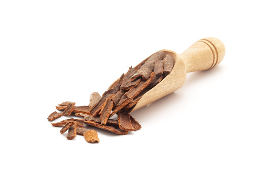 Front view of a wooden scoop filled with Organic Cinnamon sticks (Cinnamomum verum). Isolated on a white background.
