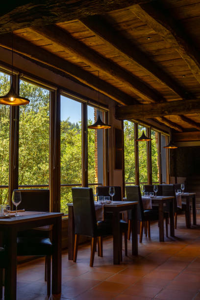 istock Rustic restaurant room of a mountain hotel, with large windows overlooking the forest and the mountains, luxuriously decorated with wooden ceiling and beams, terrazzo floor and romantic lighting. 2149209652