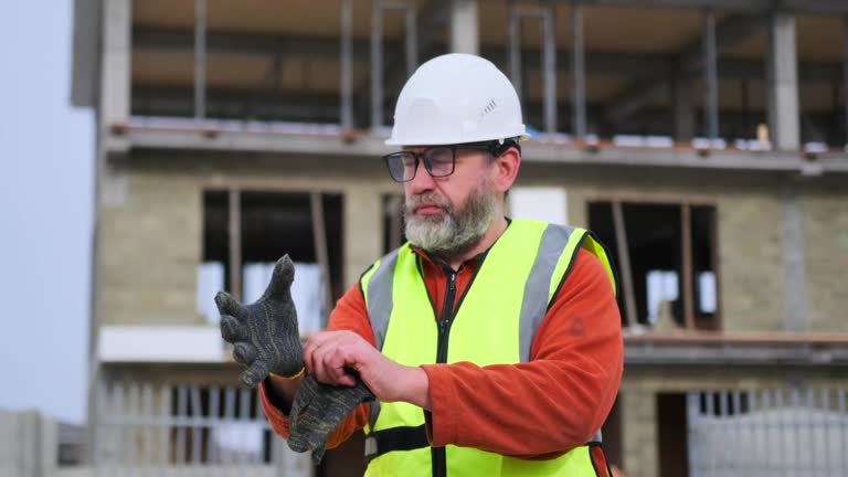 Mature age male contractor puts on work gloves while standing on a construction site