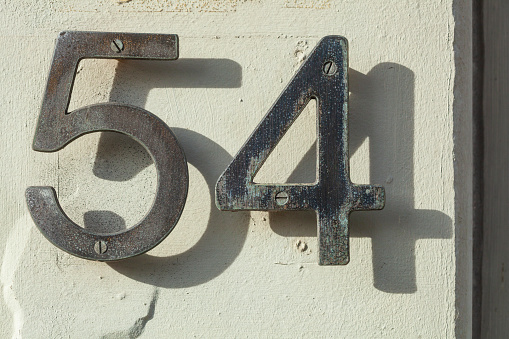 Black metal house number sign number fifty-four with shadow on a white house wall, Germany