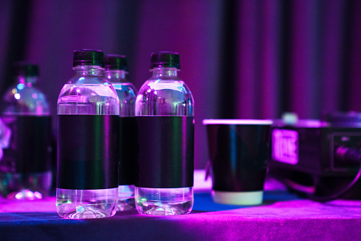 Plastic water bottles with blank black labels in the dark and purple lighting. Place for the inscription.