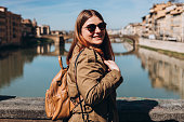 Stylish Happy Young woman enjoys beautiful view on famous Old bridge in Florence. Female traveler visiting Italian landmarks. Concept of travel, tourism and vacation in city