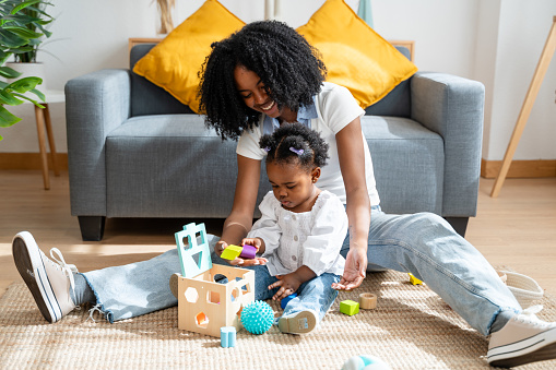 Cheerful mother engages in playtime with her toddler, building blocks together at home