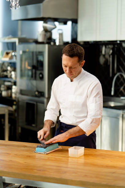 istock a chef in a white jacket in the kitchen at the table sharpens knife on a green stove 2149213204