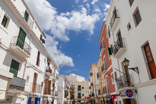 Ibiza - Spain. July 25, 2023: A charming narrow street in the heart of Eivissa town, Ibiza, Spain, lined with traditional white and colored buildings under a bright blue sky