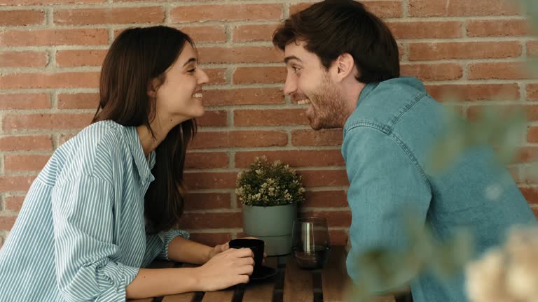 Happy couple drinking soft drink and coffee in a restaurant bar. Young people laughing happily and spending a good time chatting while sitting at the table in the daytime restaurant. Relationship -