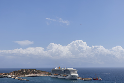 Ibiza - Spain. July 25, 2023: Anchored in the port of Eivissa on Ibiza, the grand cruise ship is a striking presence against the azure sea, under a sky filled with dramatic clouds