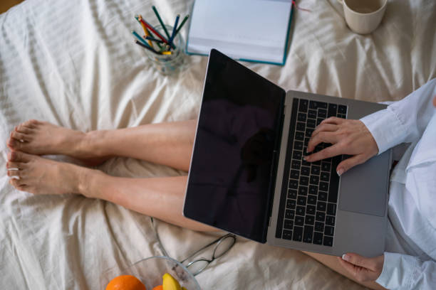 istock Woman working on laptop while sitting on the bed 2149214650