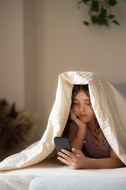 istock Sad girl using mobile phone under the blanket 2149215377