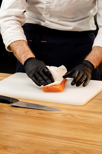 close-up of a chef's hands in black gloves dipping a salmon fillet with a napkin