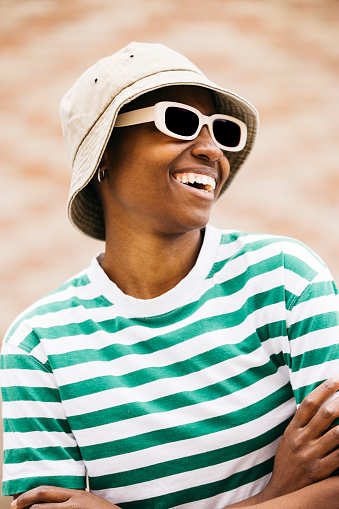 Outdoors portrait of a young cheerful woman wearing sunglasses and a hat. Young woman smiling cheerfully in an outdoor setting.