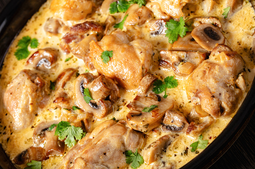 close-up of chicken thighs in a creamy mushroom garlic sauce with herbs and parmesan cheese in baking dish