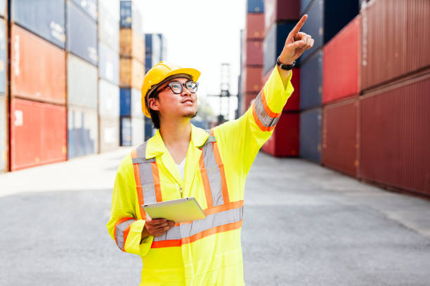 istock Asian man engineer working with tablet and point up at containers at a container yard. Shipping business management and international goods import-export. Logistic operation concept. Diversity workers 2149218936