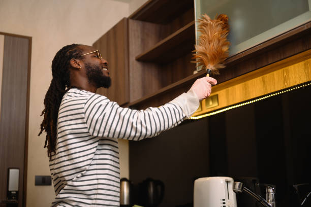 istock Happy young African man in casual clothes dusting shelf with a feather duster. 2149219091