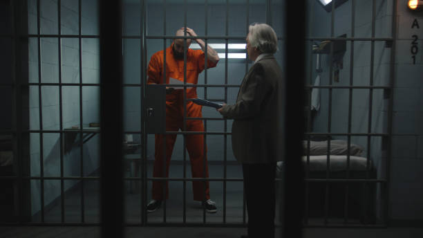 istock Prisoner in orange uniform walks behind bars in prison cell 2149219704