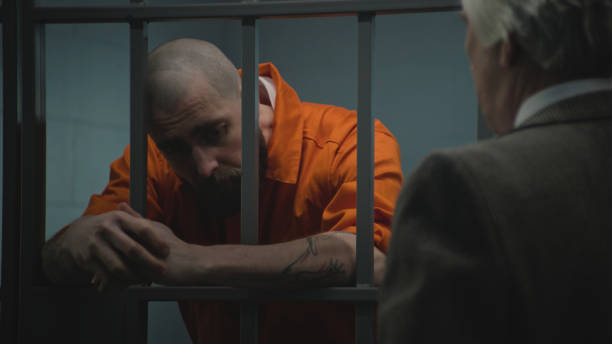 istock Prisoner in uniform stands in prison cell, talks with lawyer 2149219902