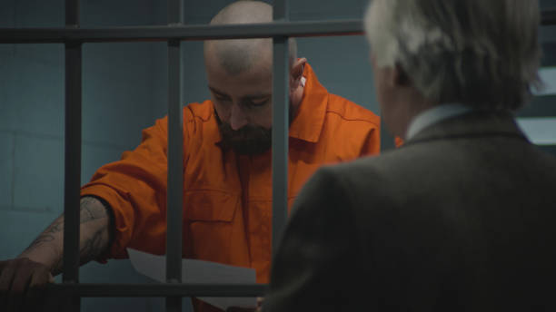 istock Prisoner in uniform stands in prison cell, talks with lawyer 2149221119