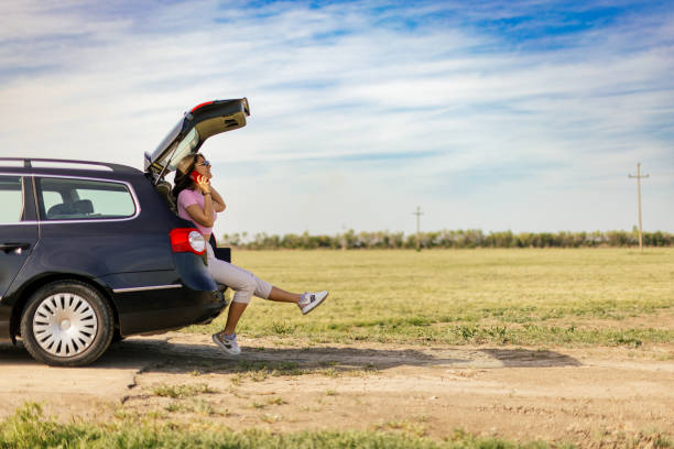 istock Young woman using mobile phone and relaxing in the car trunk 2149222002
