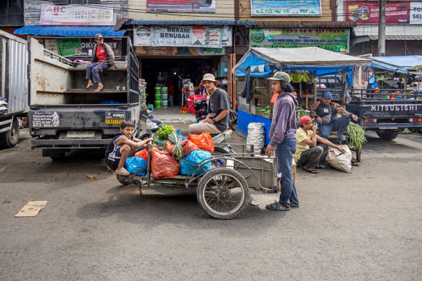 Berastagi, North Sumatra, Indonesia - January 26th 2024:  Group of young men around a motorcycle with a sidecar loaded with vegetables outside the famous green market