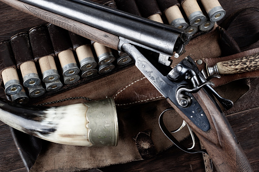 double barreled side shotgun with cartridges in bandolier on wooden table.