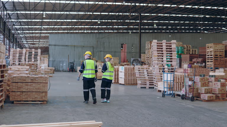 Team of industrial workers assessing lumber piles in a spacious warehouse.