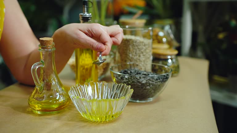 Woman pouring oil into a bowl on the tableware for a recipe. Useful properties and vitamins in sunflower oil. Close-up, a human hand evaluates the quality of sunflower oil with a spoon.