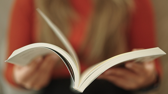Close-up hand of woman reading and open book page.