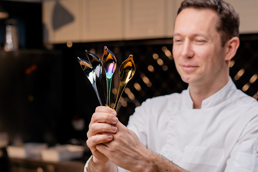 close-up of a face and chrome-plated professional spoons of tools in the hands of a chef in a professional kitchen