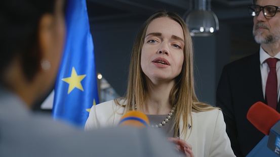 Representative of the European Union at press conference. Confident European female politician answers journalists questions, gives interview for media and television in European Parliament building.