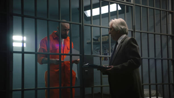 istock Criminal in orange uniform talks with lawyer and reads contract 2149225115