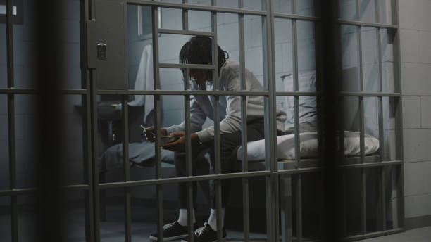 African American young prisoner eats food sitting on bed in prison cell African American young prisoner eats disgusting prison food from iron bowl sitting on bed in prison cell. Teenage criminal, inmate serves imprisonment term for crime in jail. Youth detention center. prison meal stock pictures, royalty-free photos & images