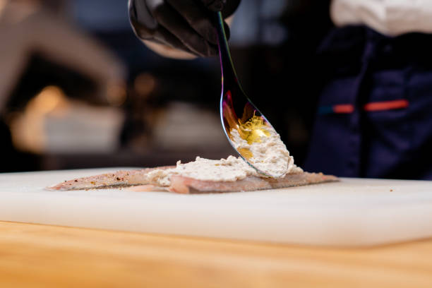 istock close-up of a chef's hands putting white sauce on fish with chrome spoon 2149227349
