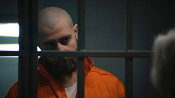 istock Criminal in orange uniform talks with lawyer and reads contract 2149228446