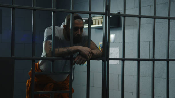 istock Inmate stands in prison cell leaning and holding hands on metal bars 2149228550