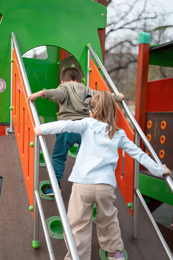 Two child friends climbing up the stairs of a playground structure, learning coordination and playfulness. Boy and a girl playing in the park