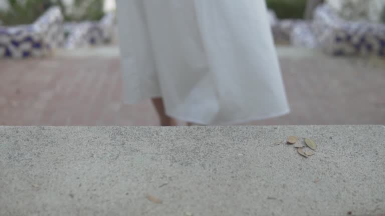 A woman in a white dress and sandals walks on the sidewalk