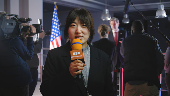 Asian anchorwoman reports breaking news live from government building. Female journalist leads broadcast for political television program from press conference with American politician or US President