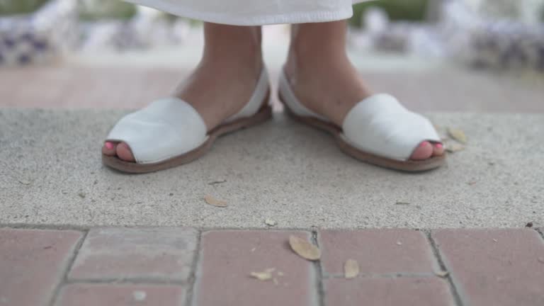 A woman, in white sandals, standing on a brick sidewalk