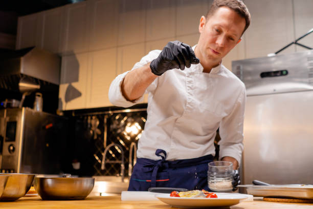 istock a chef in a white tunic in a professional kitchen sprinkles salt on finished fish dish 2149230171