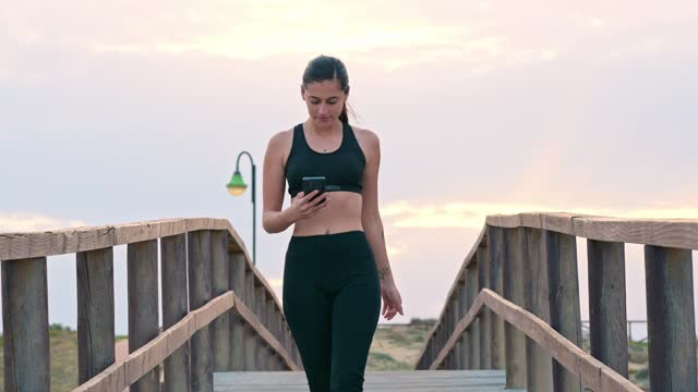 Young woman checking her phone on a wooden boardwalk at sunset