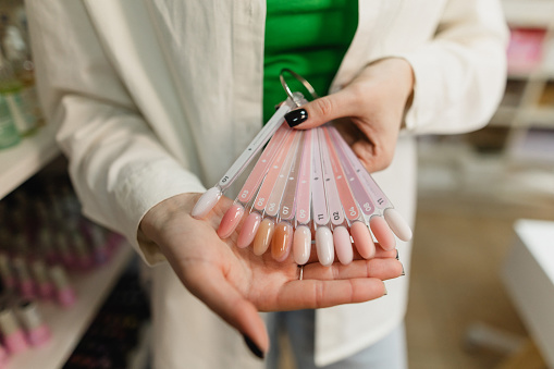 An unrecognizable manicurist offers a palette of nail polish colors. With a wide array of hues to choose from, clients are invited to explore and select the perfect shade to complement their style and preferences