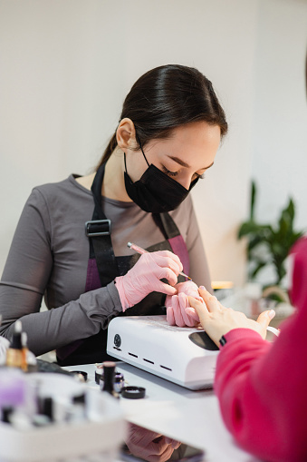 A manicurist carefully applies nail polish to a client's fingernails in the beauty salon. With skilled precision and attention to detail, they enhance the client's natural beauty, creating a flawless and elegant finish