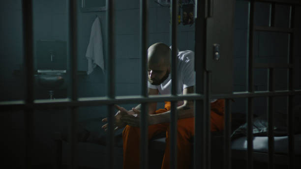 istock Criminal in orange uniform sits on bed in correctional facility 2149232609