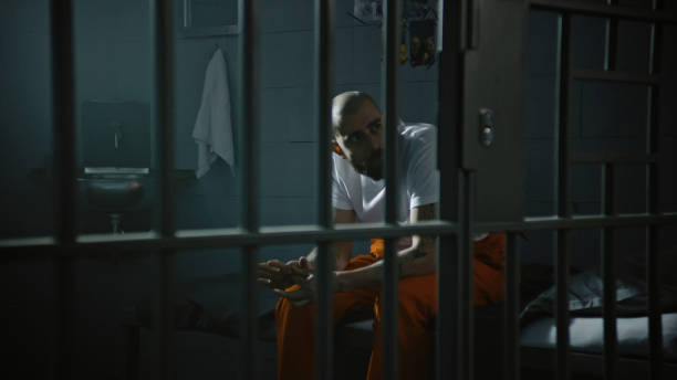 istock Criminal in orange uniform sits on bed in correctional facility 2149232980